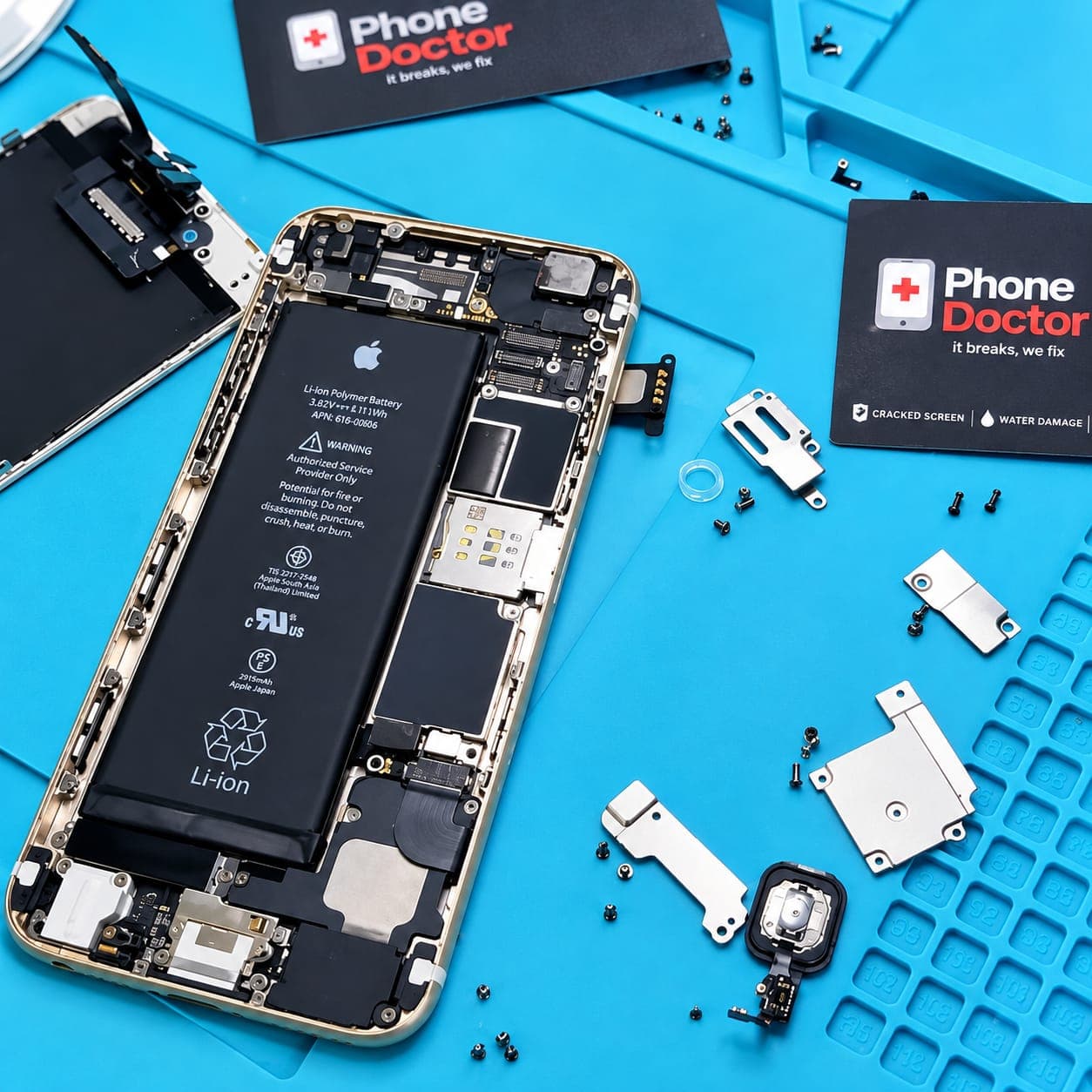 An opened iPhone with its battery and logic board exposed beside Phone Doctor branded cards