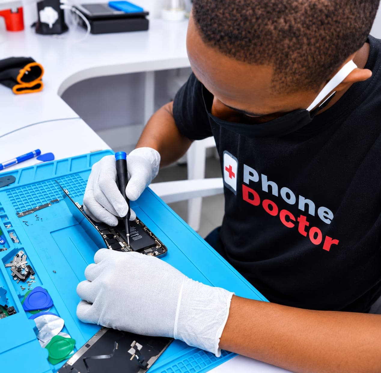 A Phone Doctor technician in gloves repairing an opened smartphone on an anti-static mat