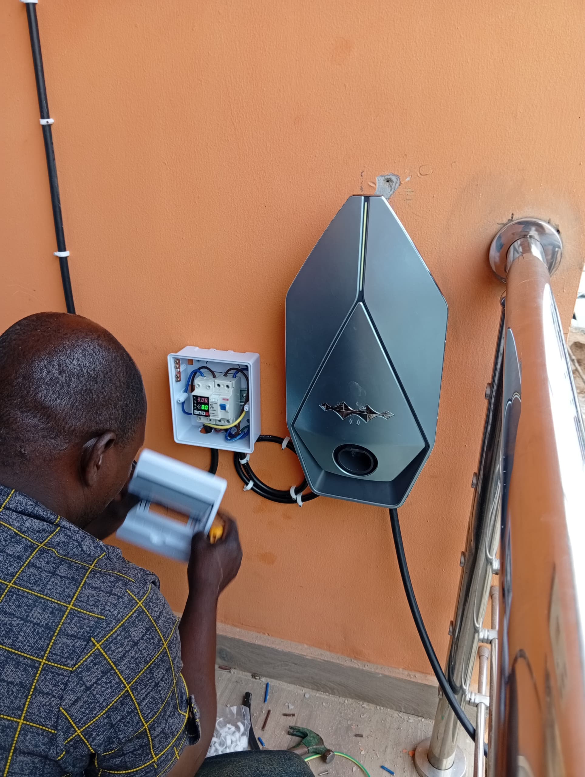 A technician wiring a protection box next to a newly wall-mounted geometric EV charger